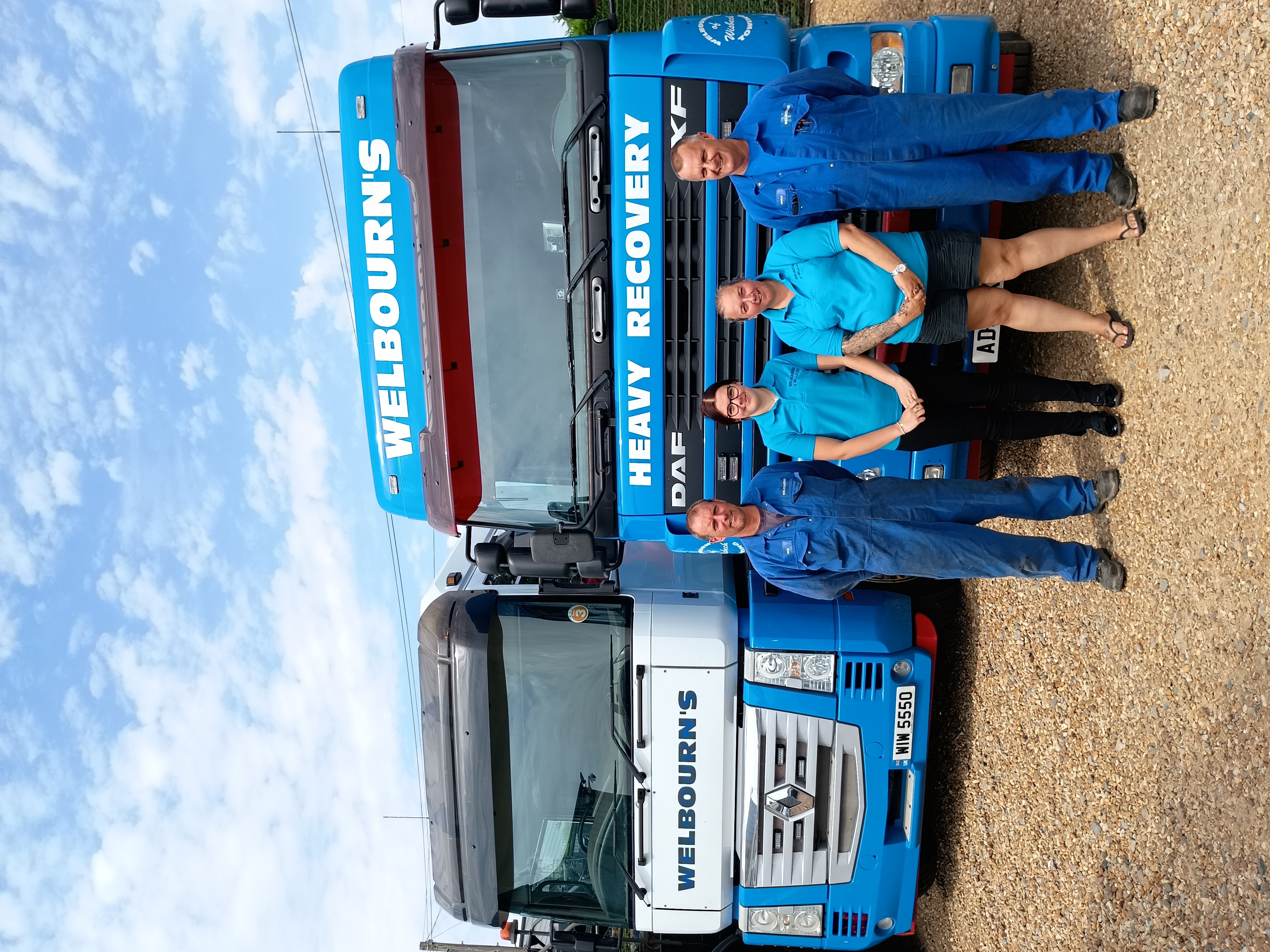 Two blue and white lorries, with four employees standing in front of them on gravel.